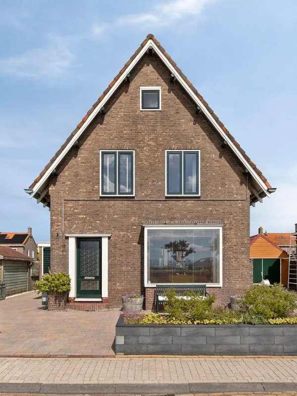 Voorgevel van een vrijstaande bakstenen woning met houten kozijnen en een erker.